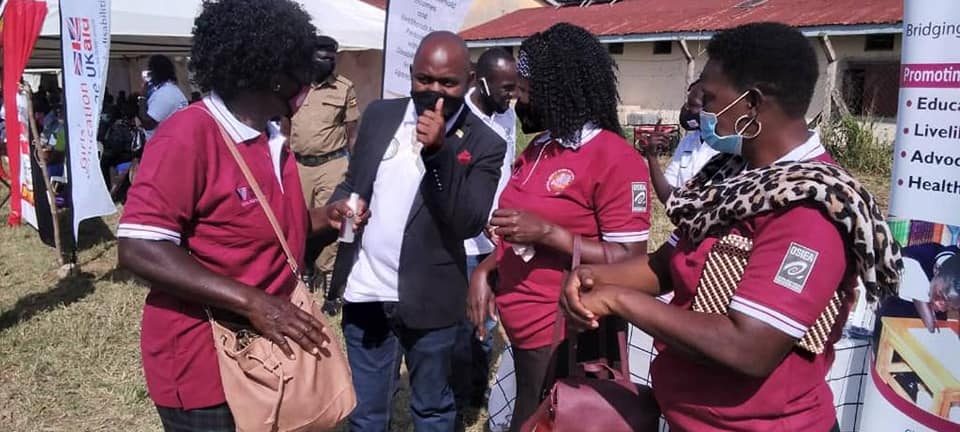 Women with hearing impairment in maroon and white collared t-shirts and black skirts standing around a man holding up the yes thumb sign