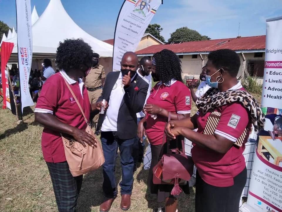 Women with hearing impairment in maroon and white collared t-shirts and black skirts standing around a man holding up the yes thumb sign